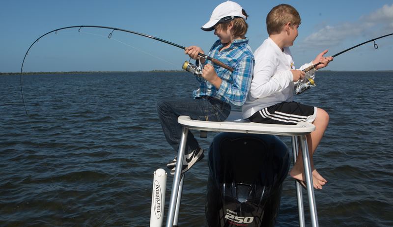 Two kids hooked up back-to-back on the poling platform of a flats boat