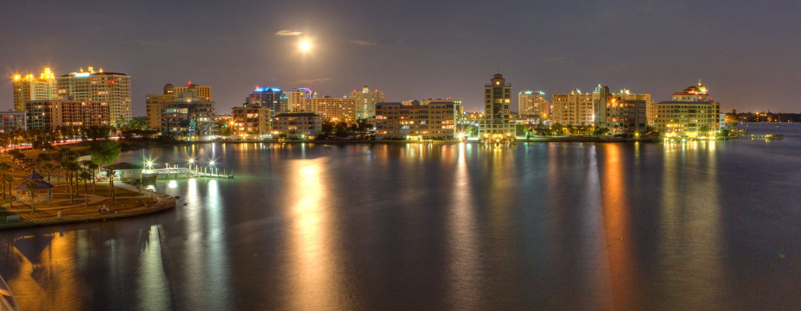 The downtown Sarasota skyline lit at night under a full moon, with light reflecting across the bay