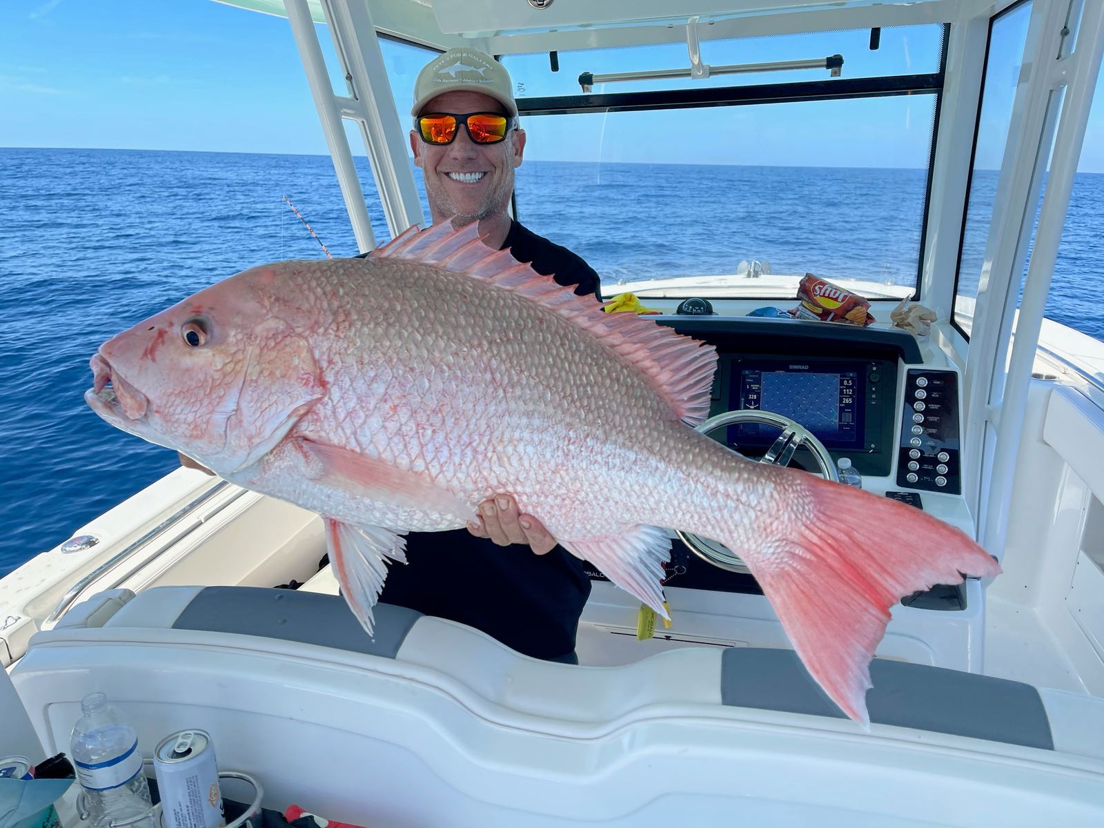 An angler at the helm holding a heavy red snapper with open Gulf water behind the boat