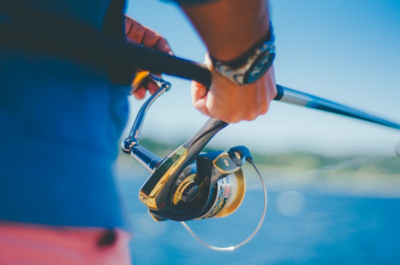 Angler in a long-sleeve sun shirt working a spinning reel on the water